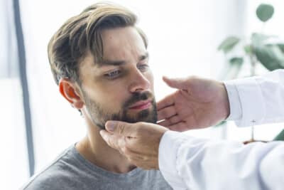 Doctor gently examining a male patient's face, focusing on the jaw area, in a medical office
