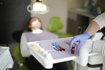 Dentist preparing dental tools on a tray while a patient is lying in a dental chair under the bright light