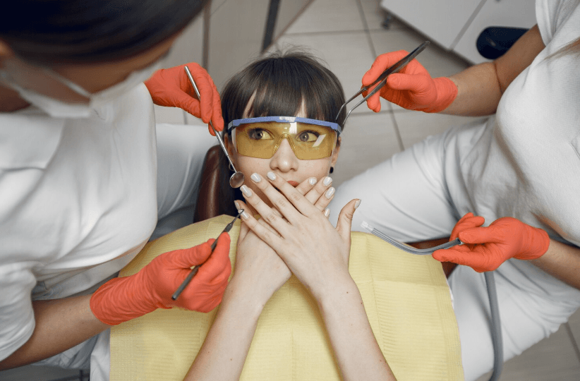 Woman sitting in a dental chair, covering her mouth with her hands