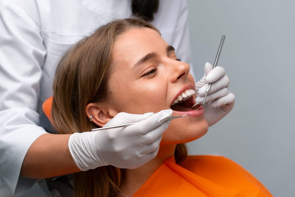 Dentist examining a young woman’s teeth with dental tools