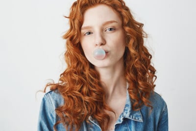 Young woman with curly red hair blowing a bubble with chewing gum