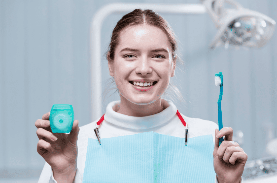 Smiling woman in a dental clinic holding dental floss and a toothbrush