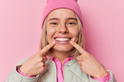 Happy woman in a pink hat pointing at her teeth with a smile