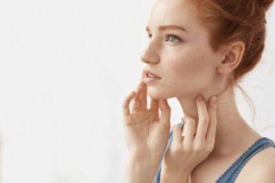 A young woman with red hair touching her neck and chin