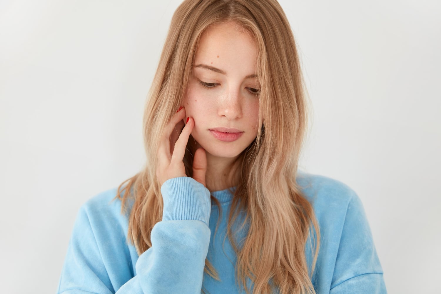 Thoughtful woman in a light blue sweater touching her cheek