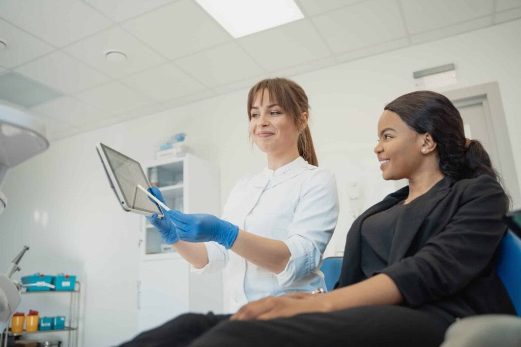 Dentist showing treatment information on a tablet to a smiling patient in a clinic.