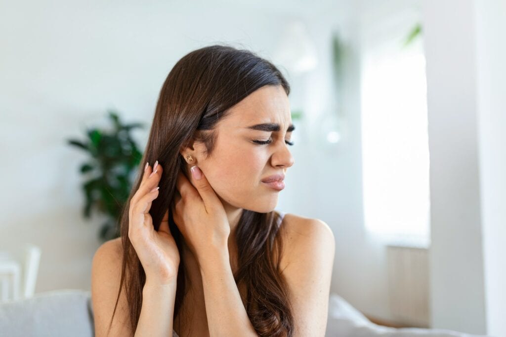 Young woman with closed eyes holding both hands near her ear and jaw
