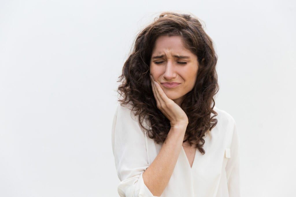 Curly-haired woman in a white blouse pressing her hand to her cheek with a distressed expression