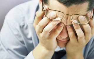 Man moving his glasses to hold his head in pain