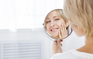 Woman touching her face while smiling at herself in a handheld mirror