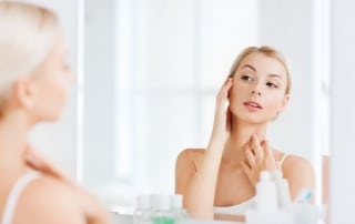 Young woman looking at herself in the mirror as she touches the side of her face and her neck