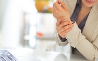 Business woman sitting in front of her computer and holding her wrist in pain